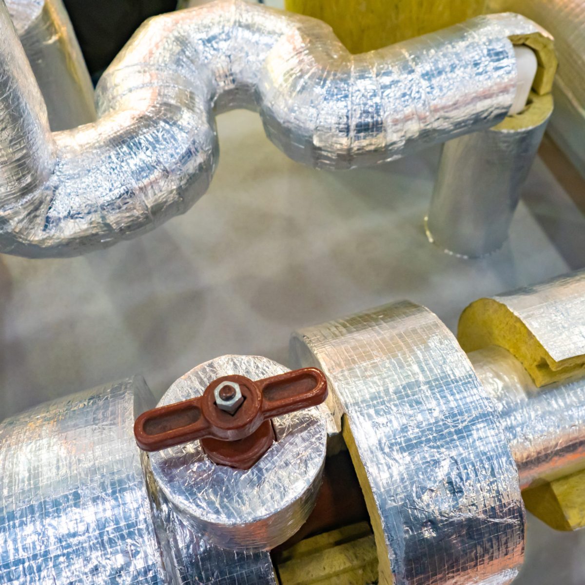 Pipes with a layer of insulating material and foil. Pipes with brown valve. Foil insulation for pipes. Demonstration of thermal insulation properties of insulation with foil.